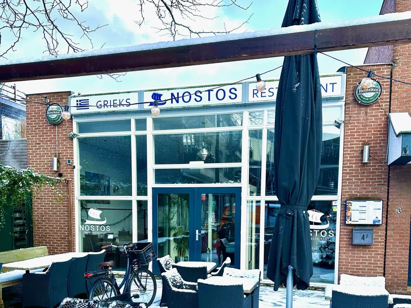 De gevel van Restaurant Nostos aan de Van Tolstraat in Bodegraven, met het terras onder een laag sneeuw