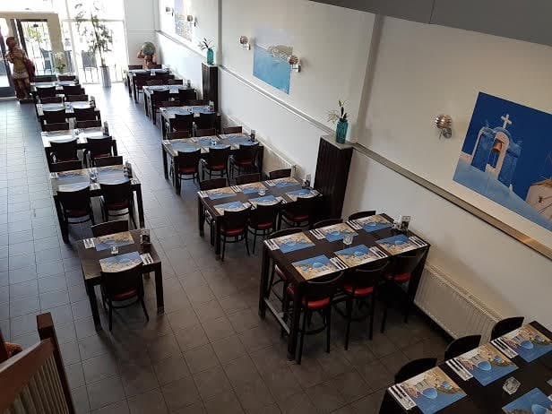 Het restaurant van Nostos van bovenaf gezien, met gedekte tafels en Griekse wanddecoratie