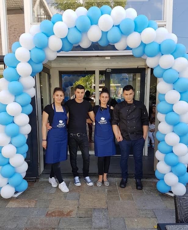 Het team van Restaurant Nostos voor de ingang met een blauw-witte ballonnenboog