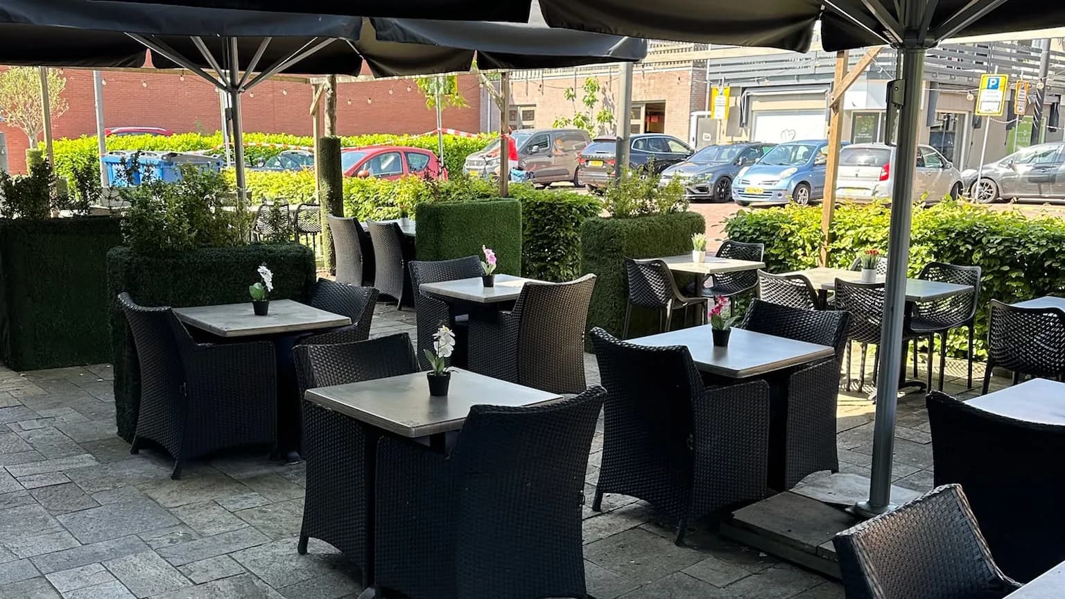 Het terras van Restaurant Nostos met zwarte parasols en gedekte tafels aan de Van Tolstraat